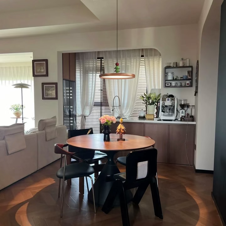 Disc pendant light with wood ring, green pine ornament and red bead above dining table