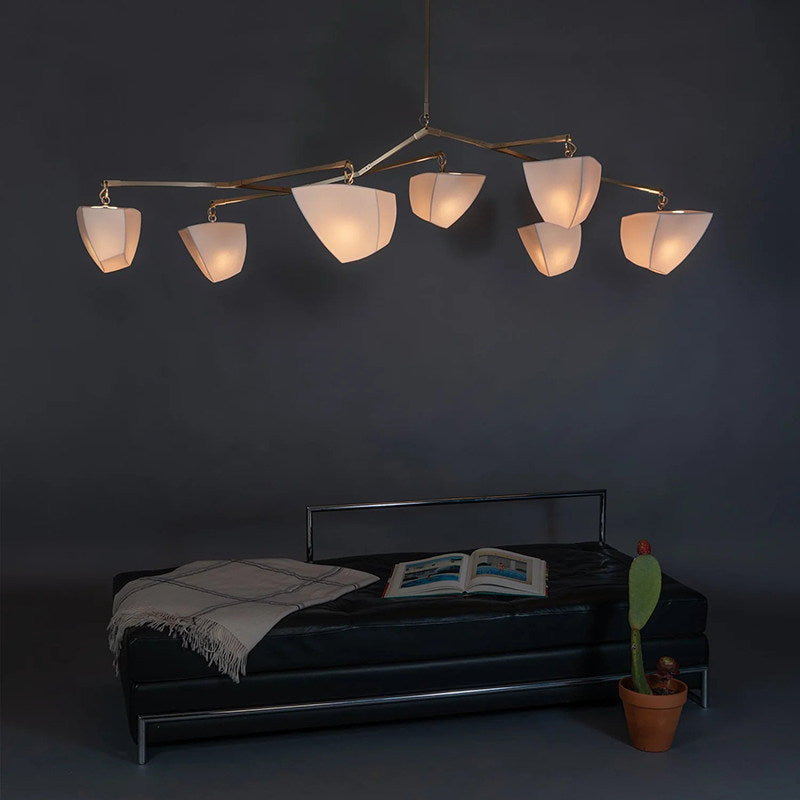 Brass branching chandelier with ten off-white cone shades glowing softly