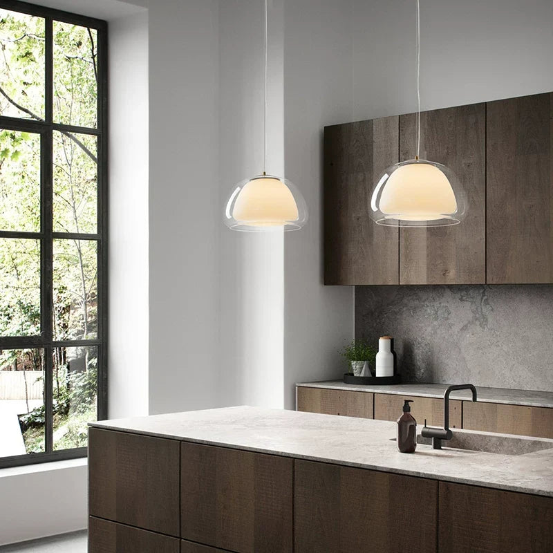 Curved glass pendant light with clear glass dome shade emitting warm ambient glow.