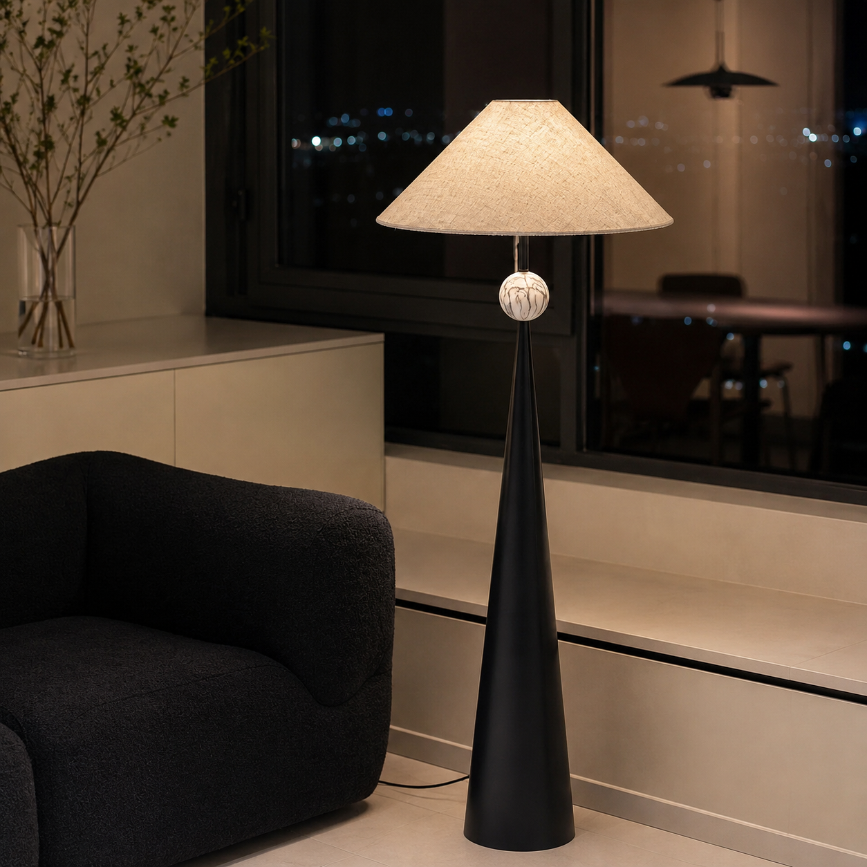 Black floor lamp with beige linen shade and spherical finial, warm-lit at night.
