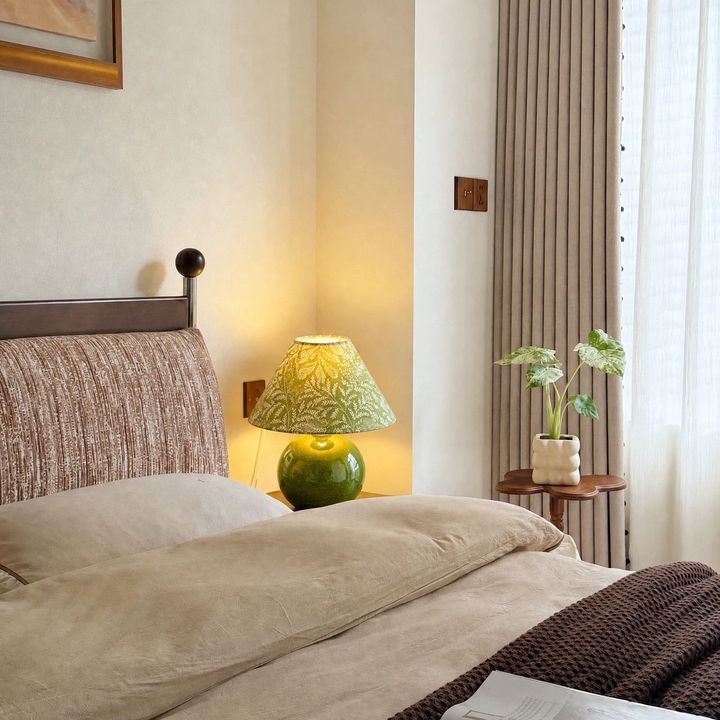Green ceramic table lamp with botanical print cone shade on bedside table