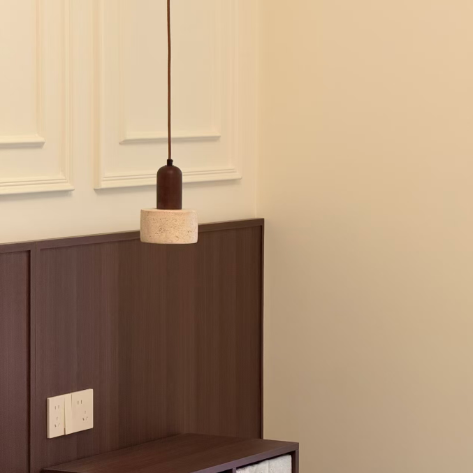 A modern bedroom corner featuring a dark brown wooden headboard and bedside storage cabinet with woven storage bins, illuminated by a hanging pendant light with a dark brown cylindrical shade and a beige textured drum shade.