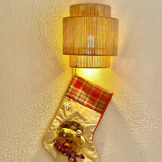 Wall-mounted rope drum sconce with warm amber glow and vertical woven texture