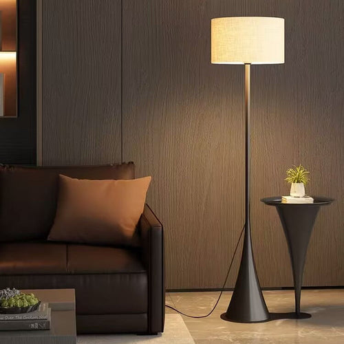 Standing floor lamp with beige fabric drum shade on a slim black stem and wide base