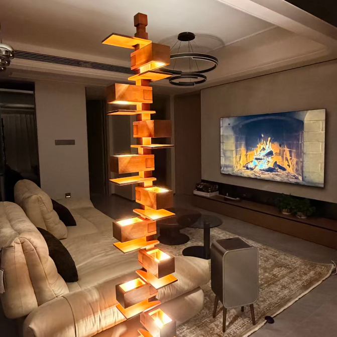 A modern living room featuring a tall, decorative wooden block tower with integrated warm LED lighting, styled in front of a cream sectional sofa and a large wall-mounted fireplace display.