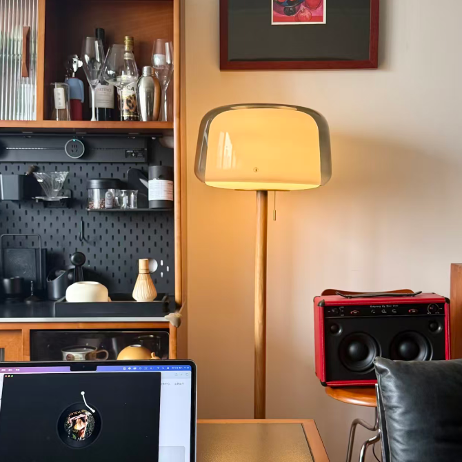 Smoked-glass floor lamp with wood stem near a bar cart and speakers