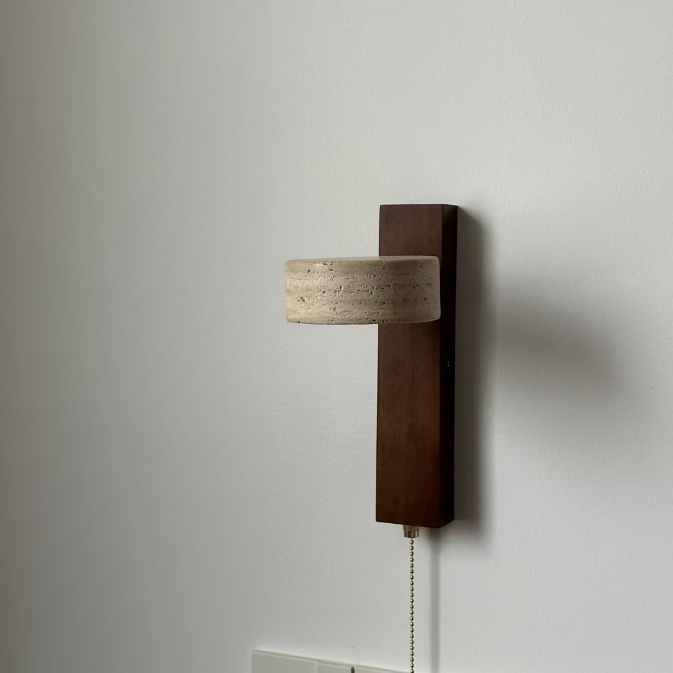 A modern wall-mounted light fixture with a dark brown wooden vertical backplate, a cylindrical beige textured shade, and a pull chain, shown against a plain off-white wall.