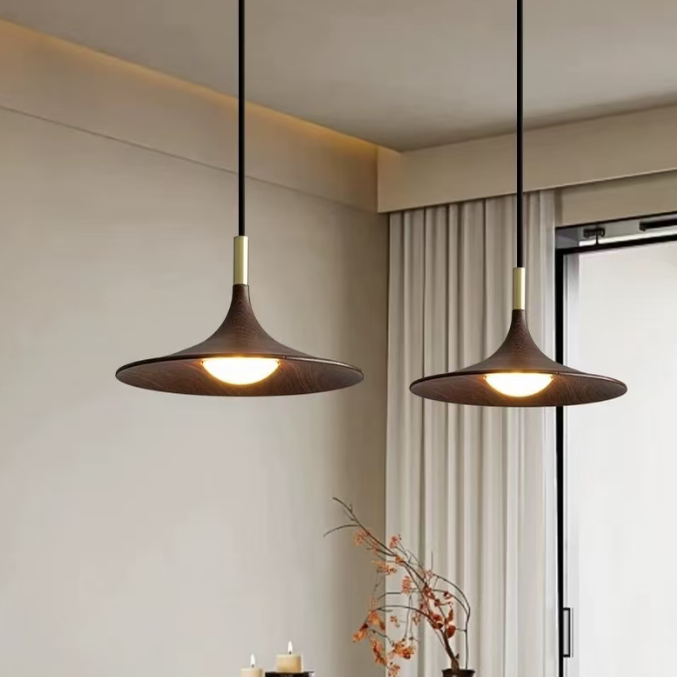 Two modern pendant lights with dark brown conical shades and gold accents hang over a wooden dining table in a warm, contemporary dining room setting.