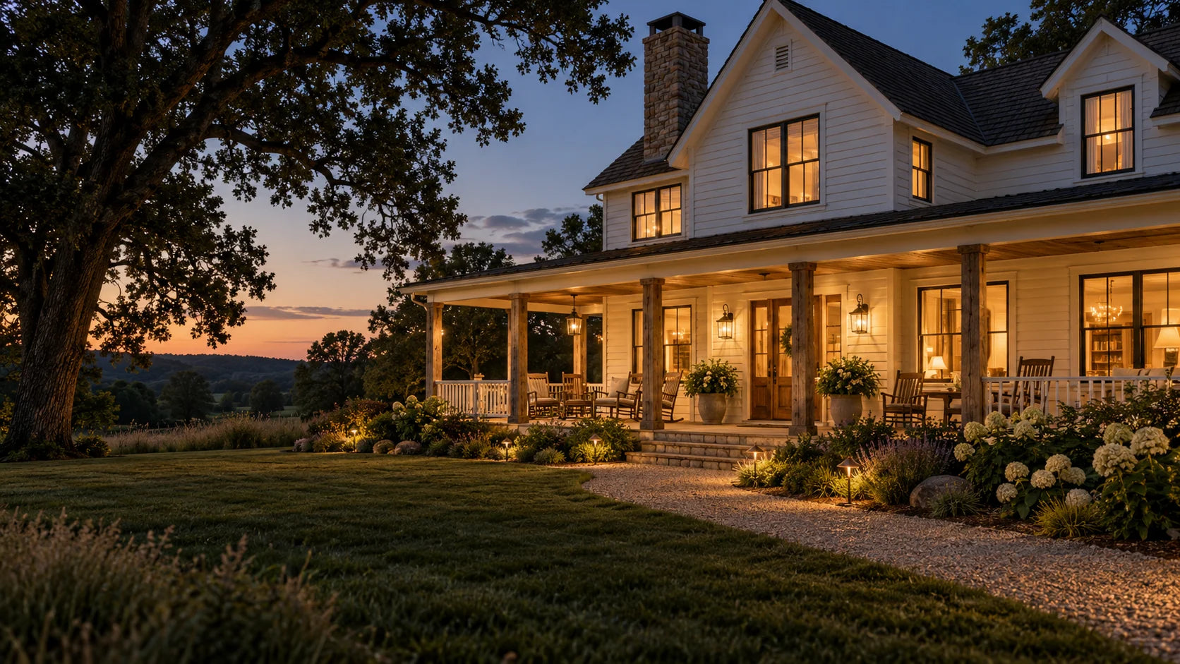 American country farmhouse exterior with a wooden porch, lawn and warmly lit windows at dusk